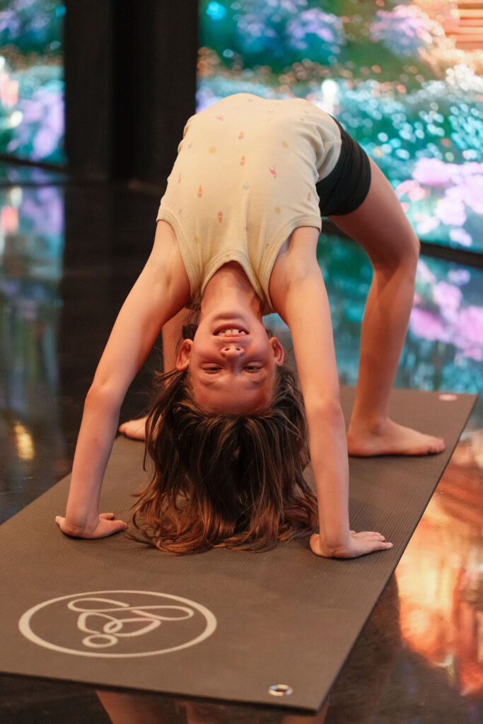Child practicing bridge pose on a yoga mat during a yoga camp for kids in an immersive studio environment